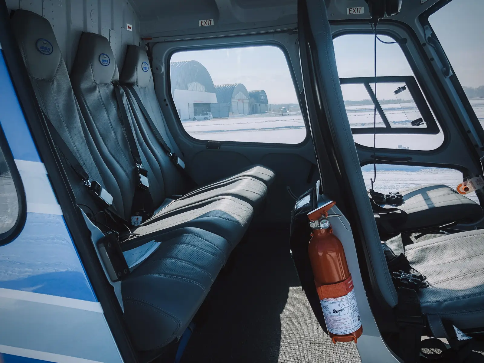 Interior cabin of a charter helicopter with passenger seats and view of the airfield hangars